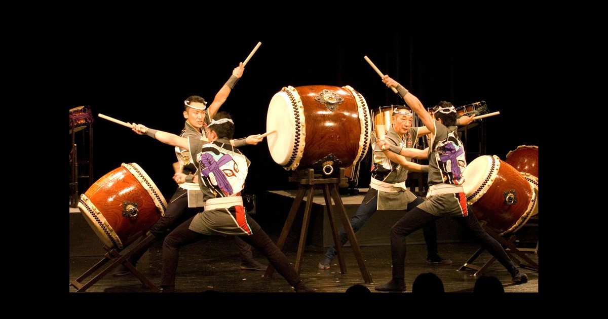 Japanese taiko performers playing large drums on a dark stage